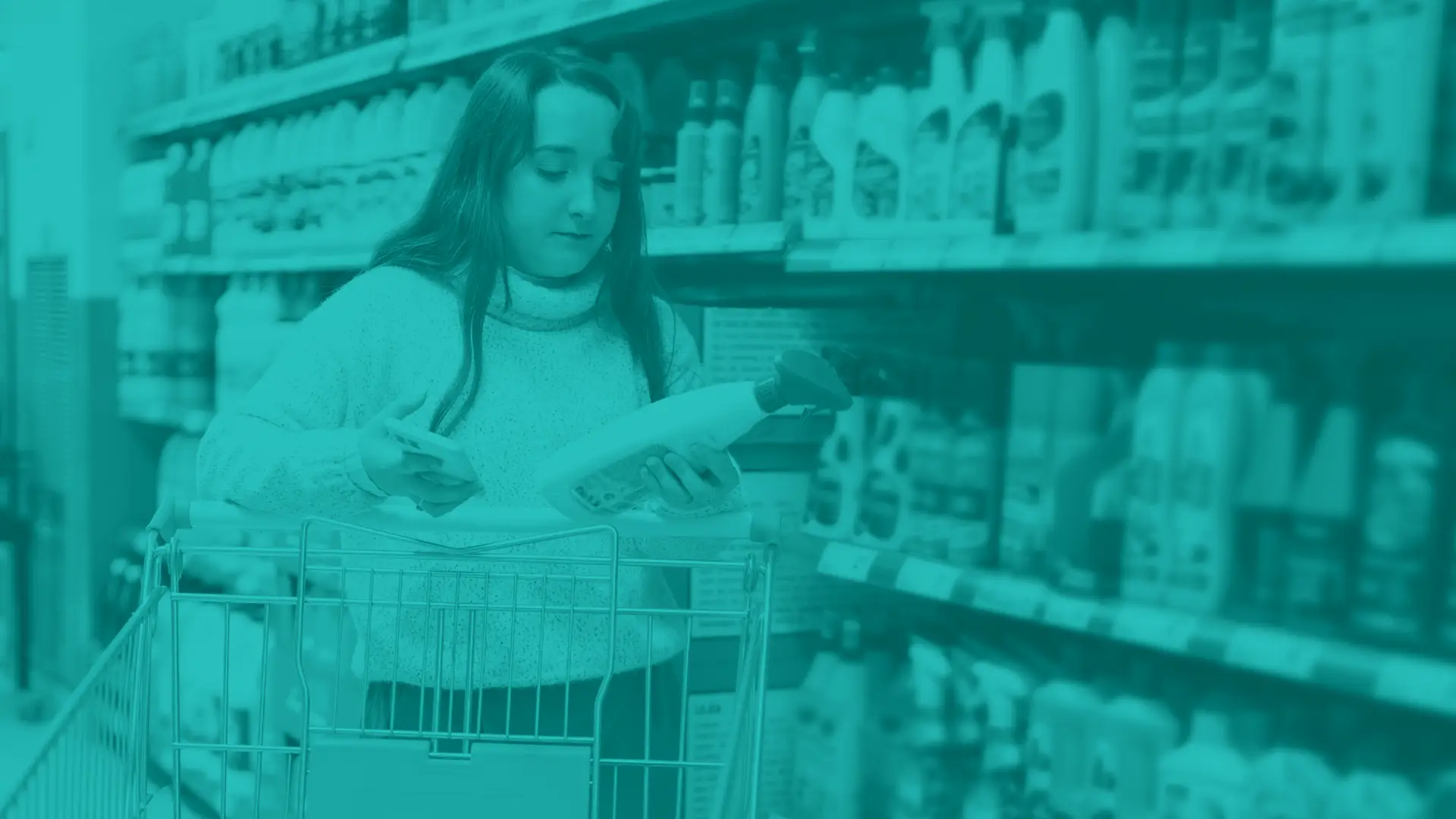 woman comparing items and using a phone while pushing a shopping cart at grocery retailer