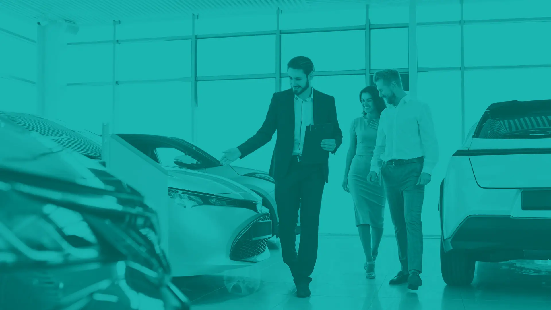 Automotive dealership salesman gesturing to new car in dealership showroom as a couple looks on shopping for a car