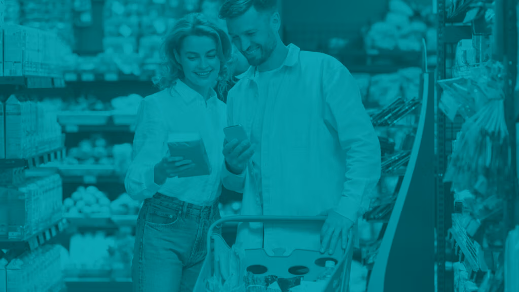 Smiling young couple in grocery store isle. Woman has a product in here hand and man is holding his smart phone, they are looking at both product and phone.