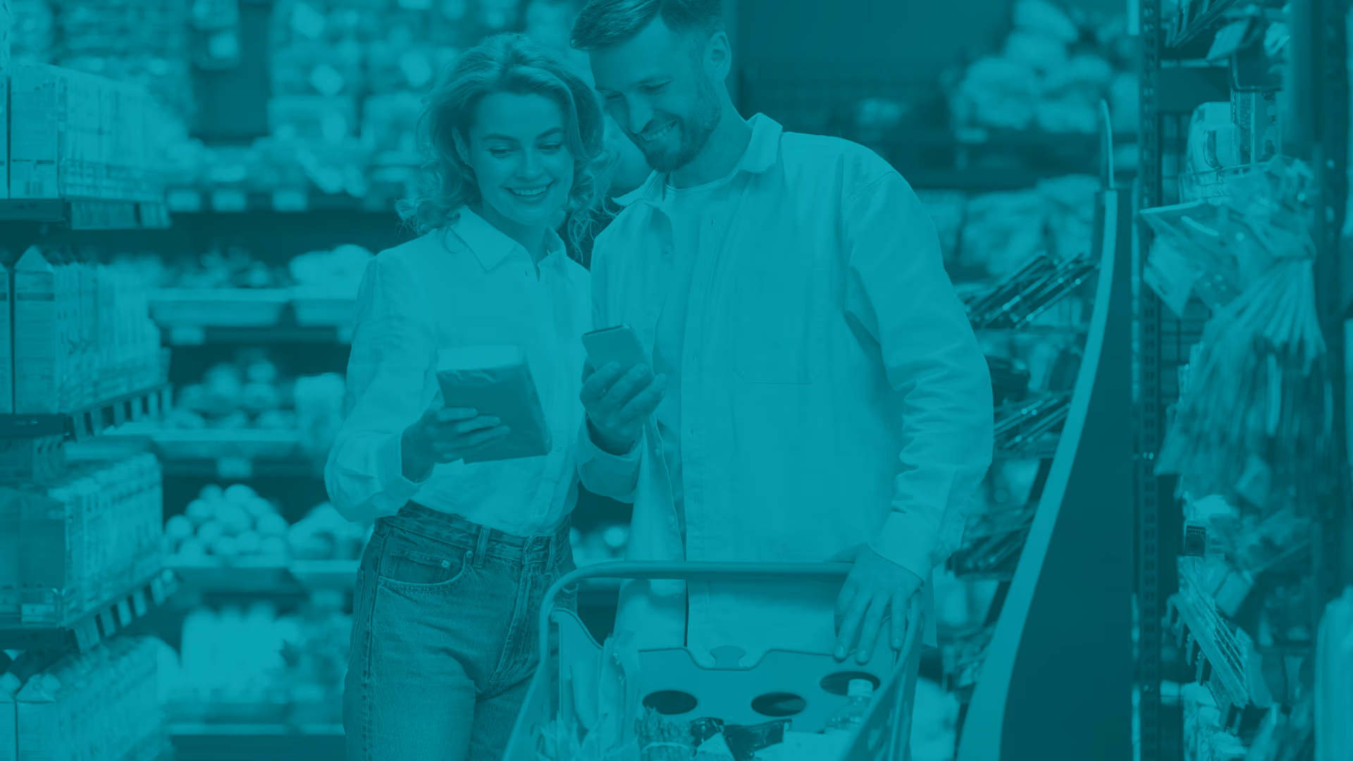 Smiling young couple in grocery store isle. Woman has a product in here hand and man is holding his smart phone, they are looking at both product and phone.