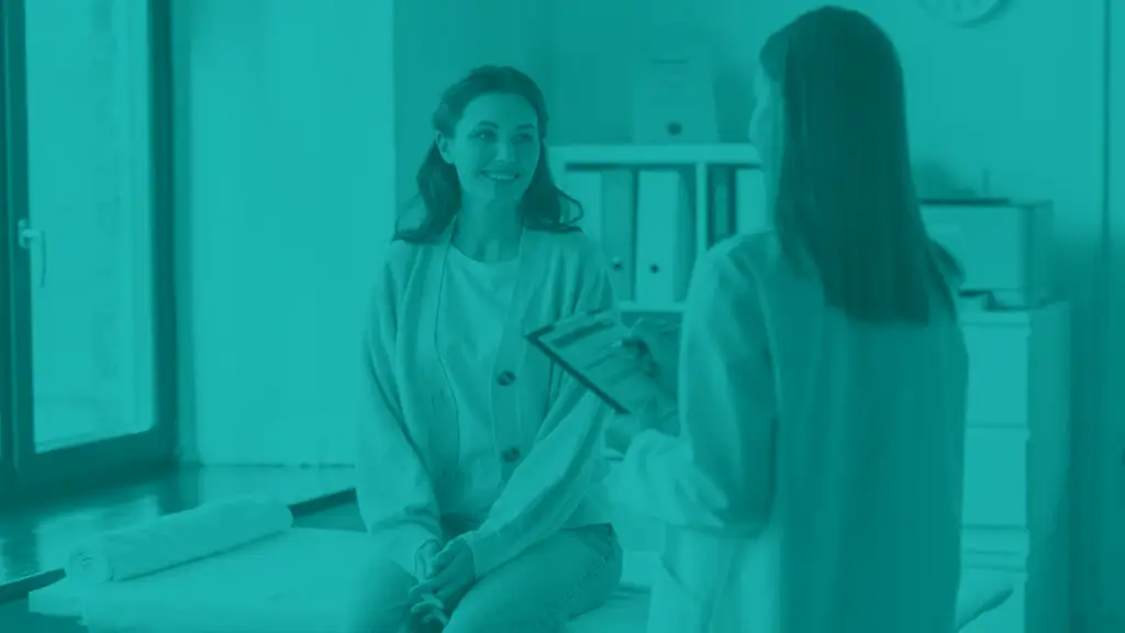 female doctor with clipboard talking to smiling woman patient at medical office