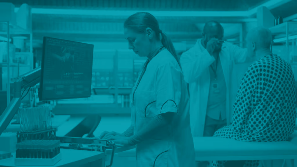 Medical clinical trial scene in a hospital or other medical facility room, nurse entering data into a computer while doctor exanims trial participant in the background.