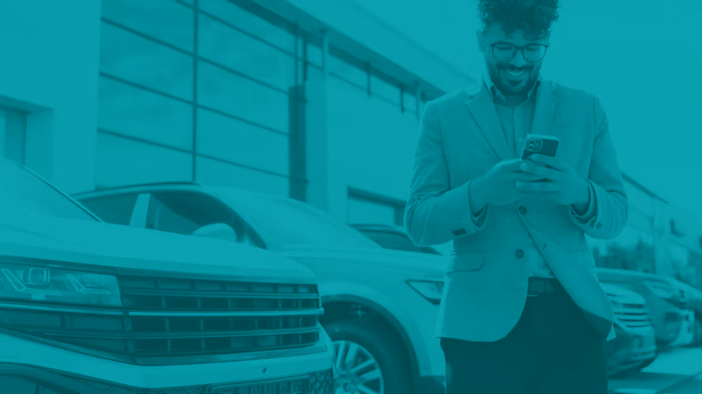 Man standing in automotive dealership parking lot near some vehicles looking at his smart phone.