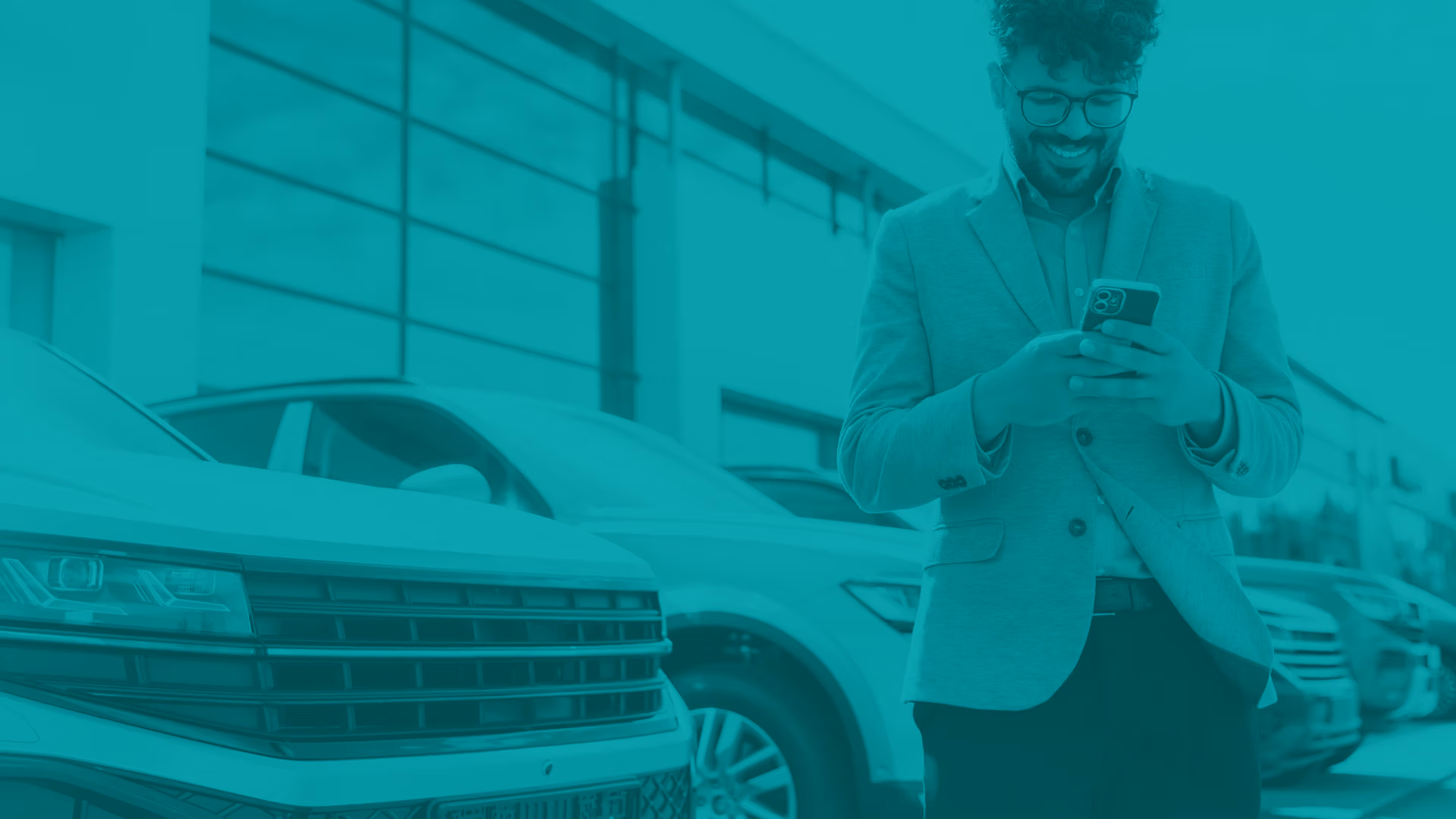 Man standing in automotive dealership parking lot near some vehicles looking at his smart phone.