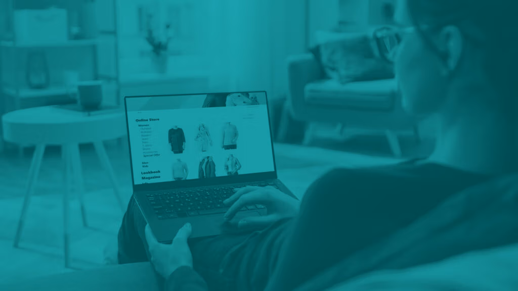 Woman sitting on couch with laptop on her lap shopping online for clothes, point of view over her shoulder looking at screen